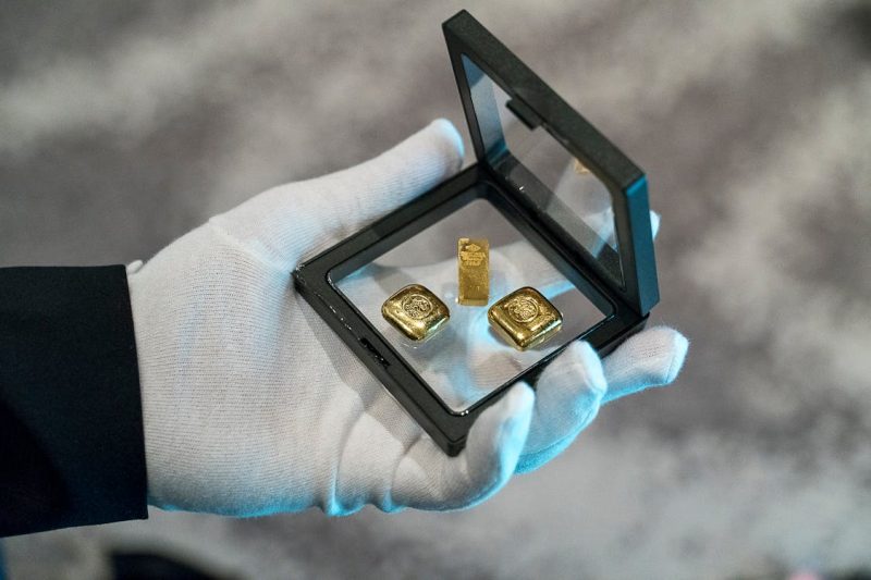 a person wearing gloves holding a glass frame with gold bars 800x533 - How to Choose the Right Gold Assets for Your Goals